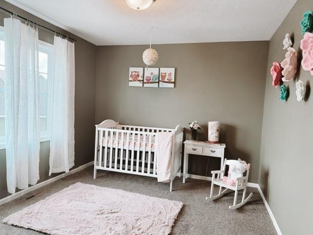 carpeted bedroom featuring a nursery area and baseboards