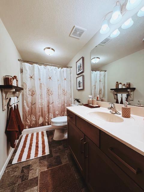 full bath featuring a textured ceiling, visible vents, toilet, and vanity