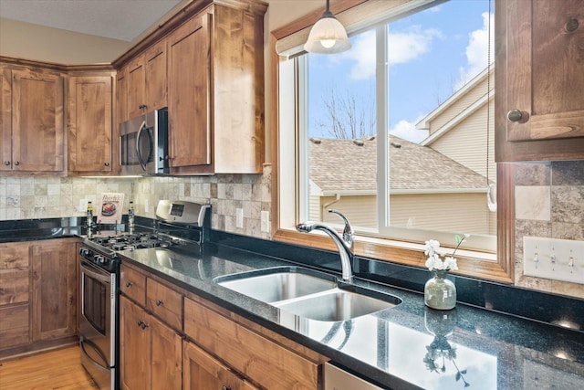 kitchen with stainless steel appliances, a sink, backsplash, brown cabinetry, and hanging light fixtures
