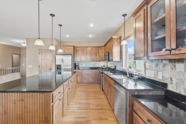 kitchen with a sink, dark stone counters, tasteful backsplash, light wood-style floors, and appliances with stainless steel finishes