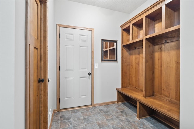 mudroom with baseboards, stone finish flooring, and a textured ceiling