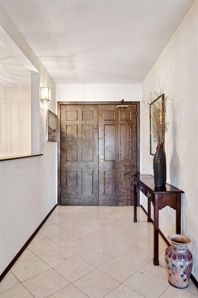 corridor with a textured wall, a textured ceiling, tile patterned floors, and baseboards