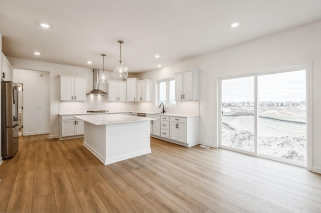 kitchen with a sink, wall chimney range hood, light countertops, freestanding refrigerator, and a kitchen island