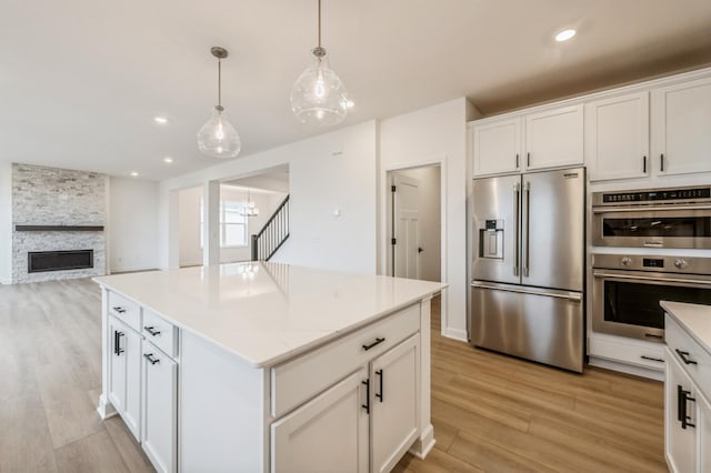 kitchen featuring stainless steel appliances, light wood-style flooring, white cabinetry, pendant lighting, and a kitchen island