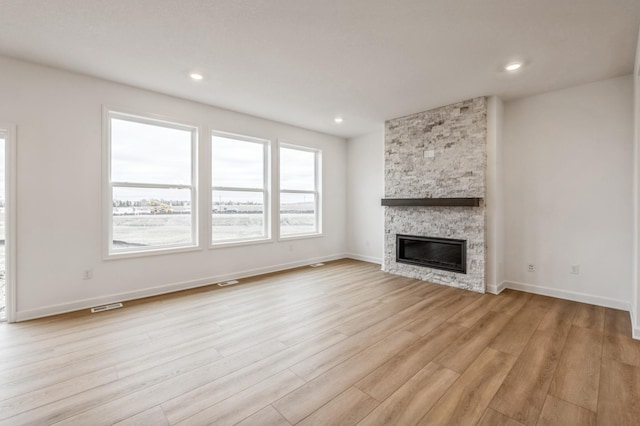 unfurnished living room featuring visible vents, a stone fireplace, light wood-type flooring, and baseboards