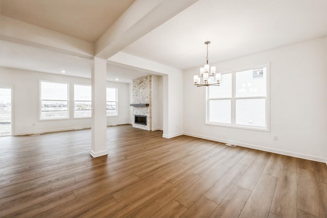 unfurnished living room featuring dark wood-style flooring, a notable chandelier, a stone fireplace, and baseboards