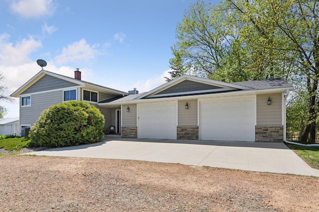 split level home featuring driveway, an attached garage, a chimney, stone siding, and cooling unit
