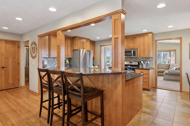 kitchen with appliances with stainless steel finishes, tasteful backsplash, recessed lighting, a breakfast bar, and a sink