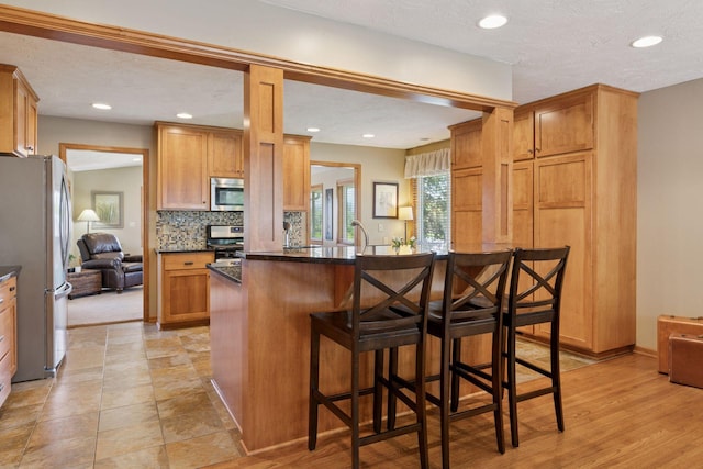 kitchen with appliances with stainless steel finishes, a breakfast bar, decorative backsplash, recessed lighting, and baseboards