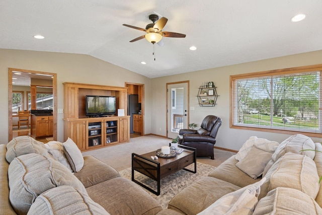 living area featuring lofted ceiling, ceiling fan, healthy amount of natural light, baseboards, and light colored carpet