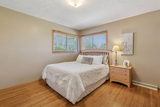 bedroom featuring a baseboard heating unit, baseboards, light wood-style flooring, and a textured ceiling