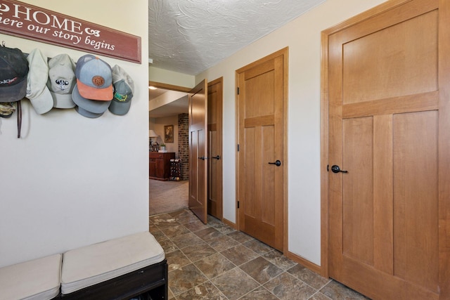 hall with dark stone finish floors, baseboards, and a textured ceiling