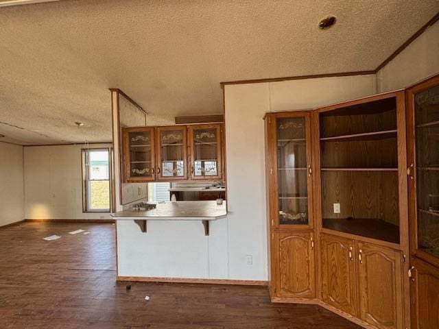 kitchen with a kitchen bar, dark wood-style flooring, a textured ceiling, and glass insert cabinets