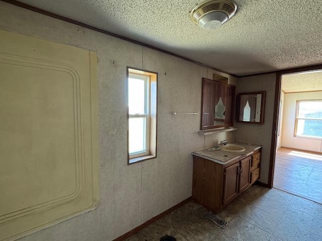 kitchen with a textured ceiling, a sink, visible vents, light countertops, and ornamental molding