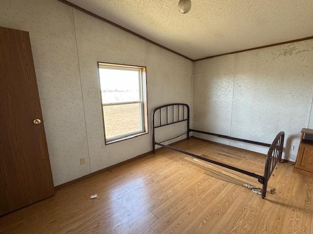 spare room with lofted ceiling, wood finished floors, a textured ceiling, and crown molding