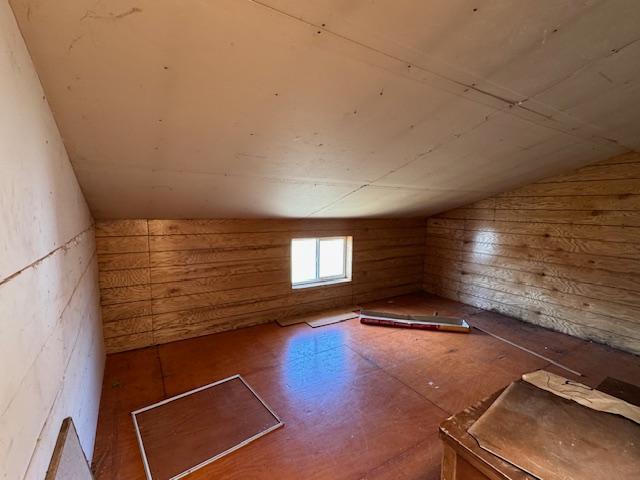 bonus room featuring vaulted ceiling and wood walls