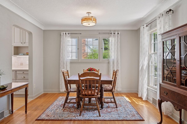 dining space featuring light wood-style flooring, a textured ceiling, crown molding, and baseboards