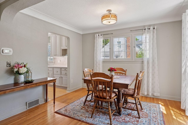 dining room featuring light wood-type flooring, arched walkways, a textured ceiling, and baseboards