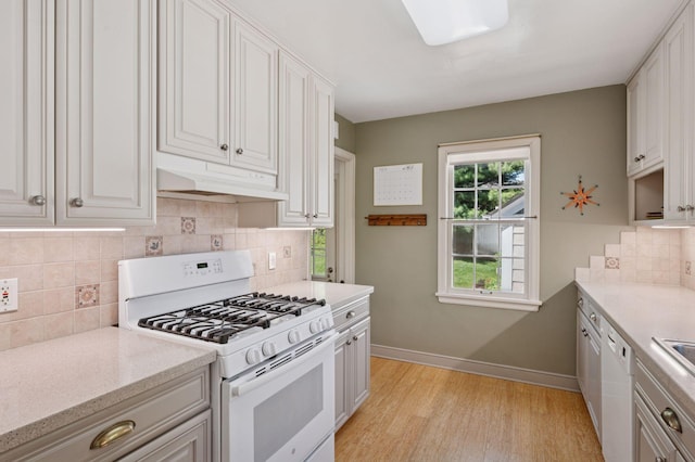 kitchen with white appliances, under cabinet range hood, light wood-type flooring, baseboards, and tasteful backsplash