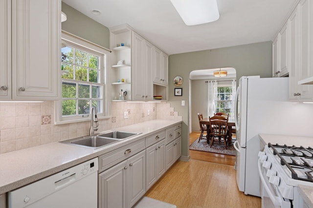 kitchen with white appliances, a sink, open shelves, arched walkways, and light wood-type flooring