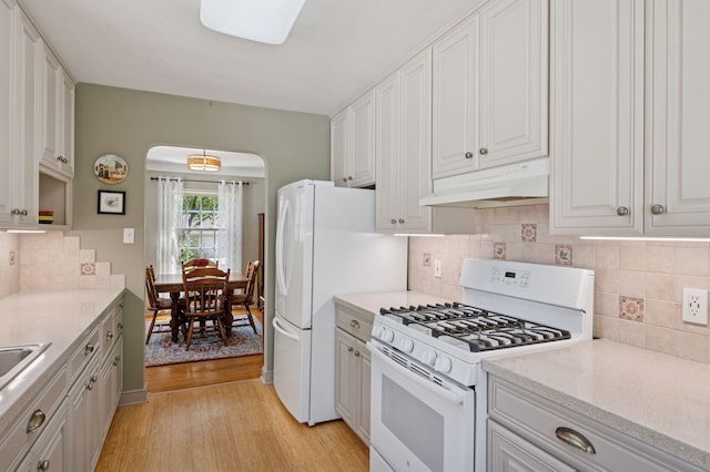 kitchen featuring white appliances, under cabinet range hood, light wood finished floors, arched walkways, and white cabinetry
