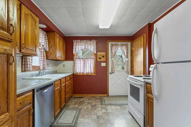 kitchen with white appliances, light countertops, brown cabinets, stone finish flooring, and a sink