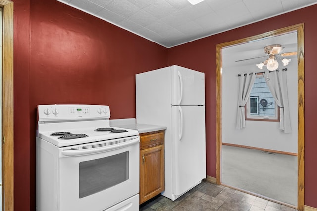 kitchen featuring stone finish floor, brown cabinets, light countertops, baseboards, and white appliances