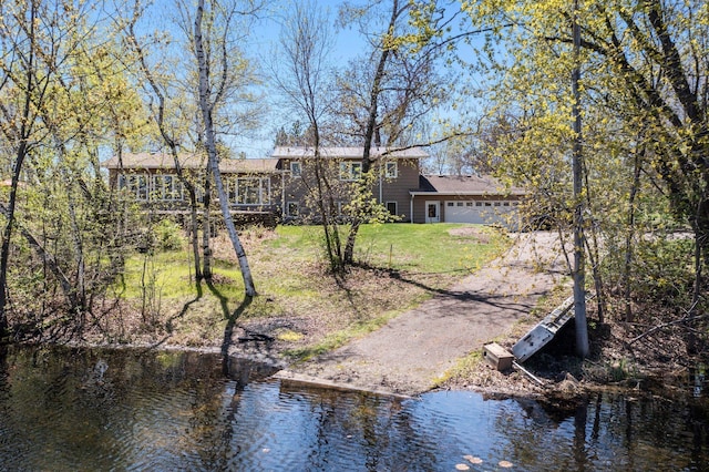 rear view of house featuring a yard, a garage, driveway, and a water view