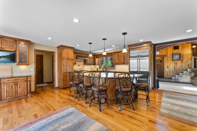 kitchen featuring a kitchen bar, built in refrigerator, light wood-style floors, brown cabinetry, and recessed lighting