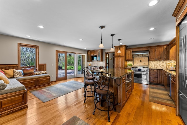 kitchen featuring appliances with stainless steel finishes, open floor plan, a breakfast bar area, dark stone countertops, and range hood
