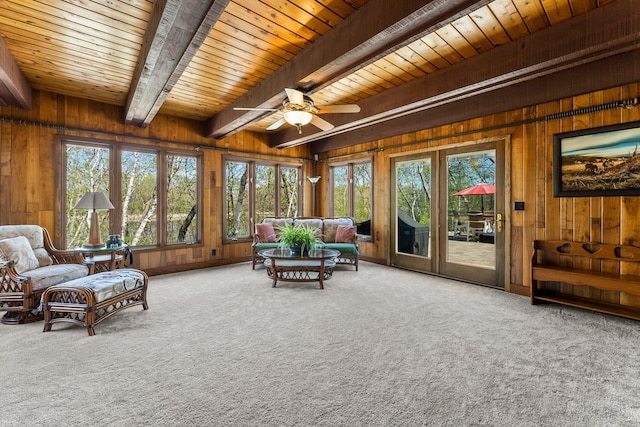 living room featuring wood walls, beam ceiling, carpet floors, plenty of natural light, and a ceiling fan