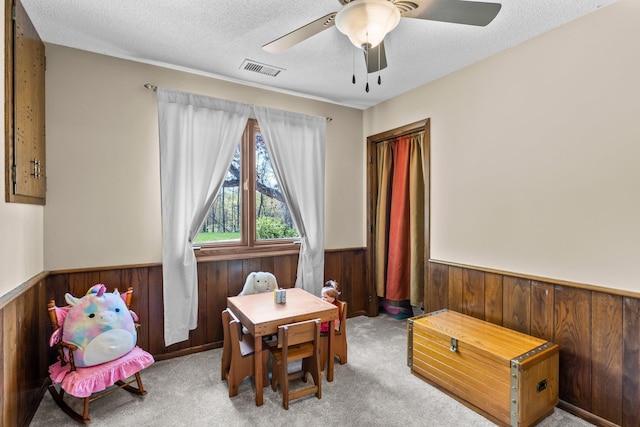 rec room with wooden walls, a wainscoted wall, a ceiling fan, carpet, and a textured ceiling