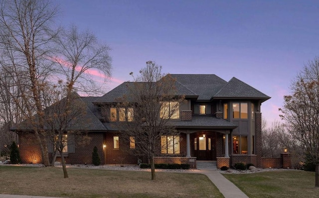 view of front facade featuring a yard, a porch, brick siding, and a shingled roof