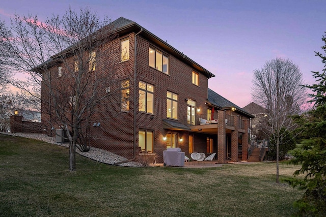 back of house at dusk with a lawn, a patio area, and a balcony