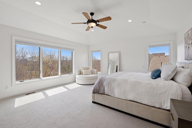 carpeted bedroom featuring vaulted ceiling, multiple windows, visible vents, and a ceiling fan