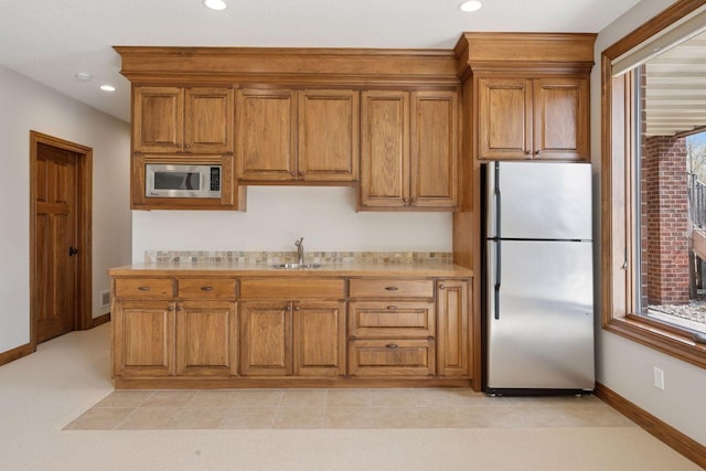 kitchen featuring light countertops, stainless steel appliances, brown cabinetry, and baseboards