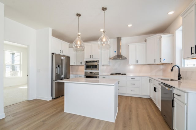 kitchen featuring stainless steel appliances, a sink, light wood-style floors, and wall chimney range hood