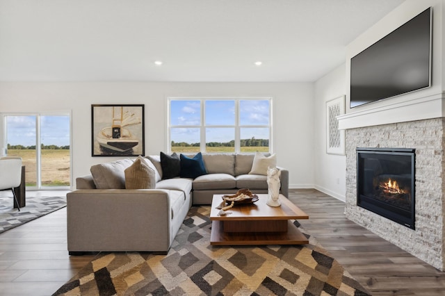 living area featuring recessed lighting, wood finished floors, baseboards, and a stone fireplace