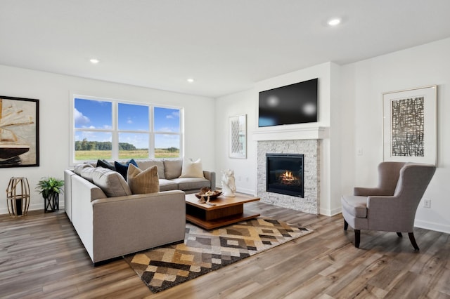 living room featuring recessed lighting, a stone fireplace, wood finished floors, and baseboards