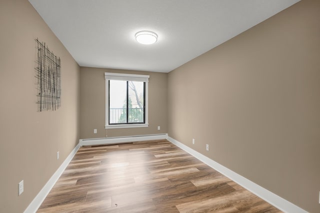 unfurnished room with baseboard heating, baseboards, and wood finished floors