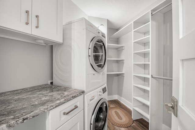 washroom featuring stacked washer and clothes dryer, dark wood-style flooring, cabinet space, and baseboards