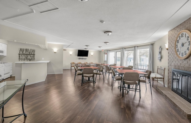 dining space with dark wood-type flooring, a brick fireplace, baseboards, and a textured ceiling