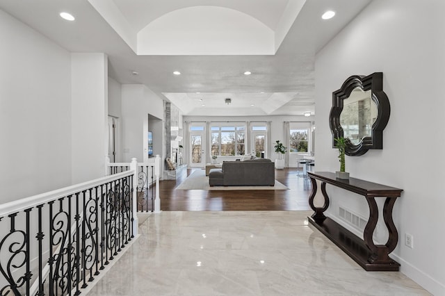 hallway with a raised ceiling, baseboards, recessed lighting, and an upstairs landing
