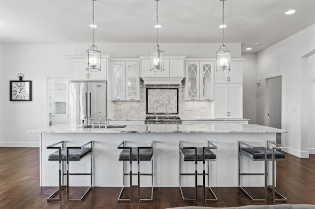 kitchen featuring a sink, baseboards, a large island with sink, high end refrigerator, and range