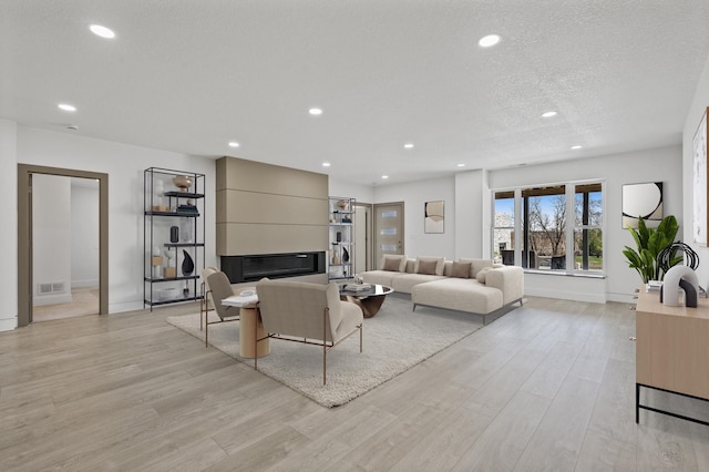 living area featuring light wood-style floors, a large fireplace, recessed lighting, and visible vents