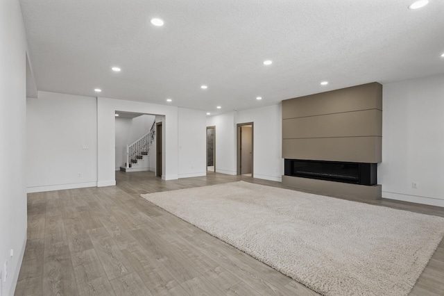 unfurnished living room with a fireplace, baseboards, stairway, recessed lighting, and light wood finished floors