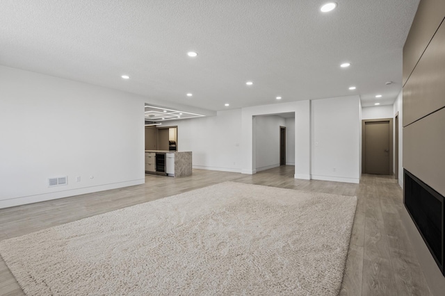 unfurnished living room featuring recessed lighting, a textured ceiling, visible vents, and light wood finished floors