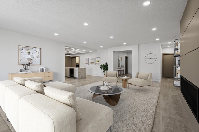 living area with recessed lighting, a textured ceiling, light wood-style flooring, and baseboards