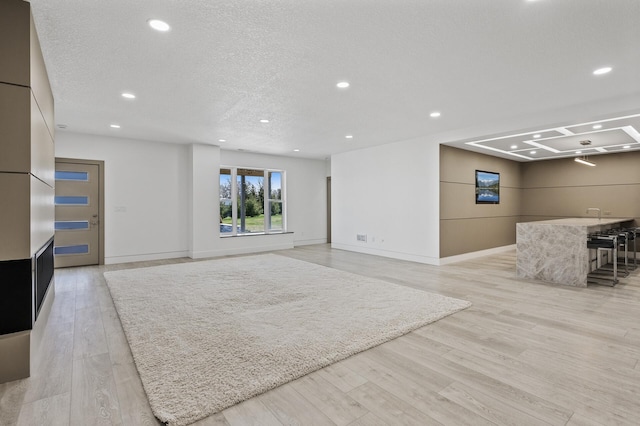 basement featuring recessed lighting, a textured ceiling, light wood finished floors, and baseboards