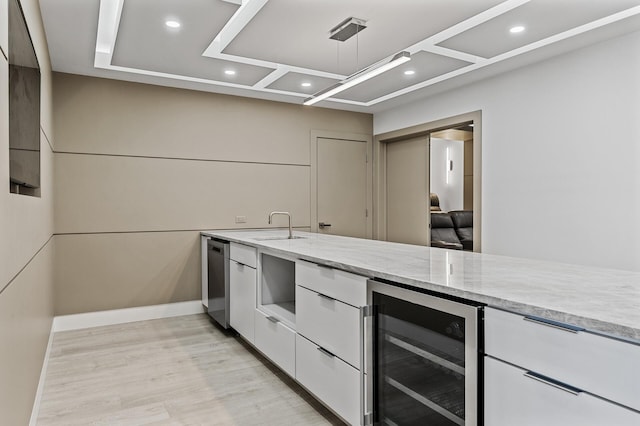 kitchen featuring wine cooler, white cabinets, light stone counters, a sink, and light wood-style flooring